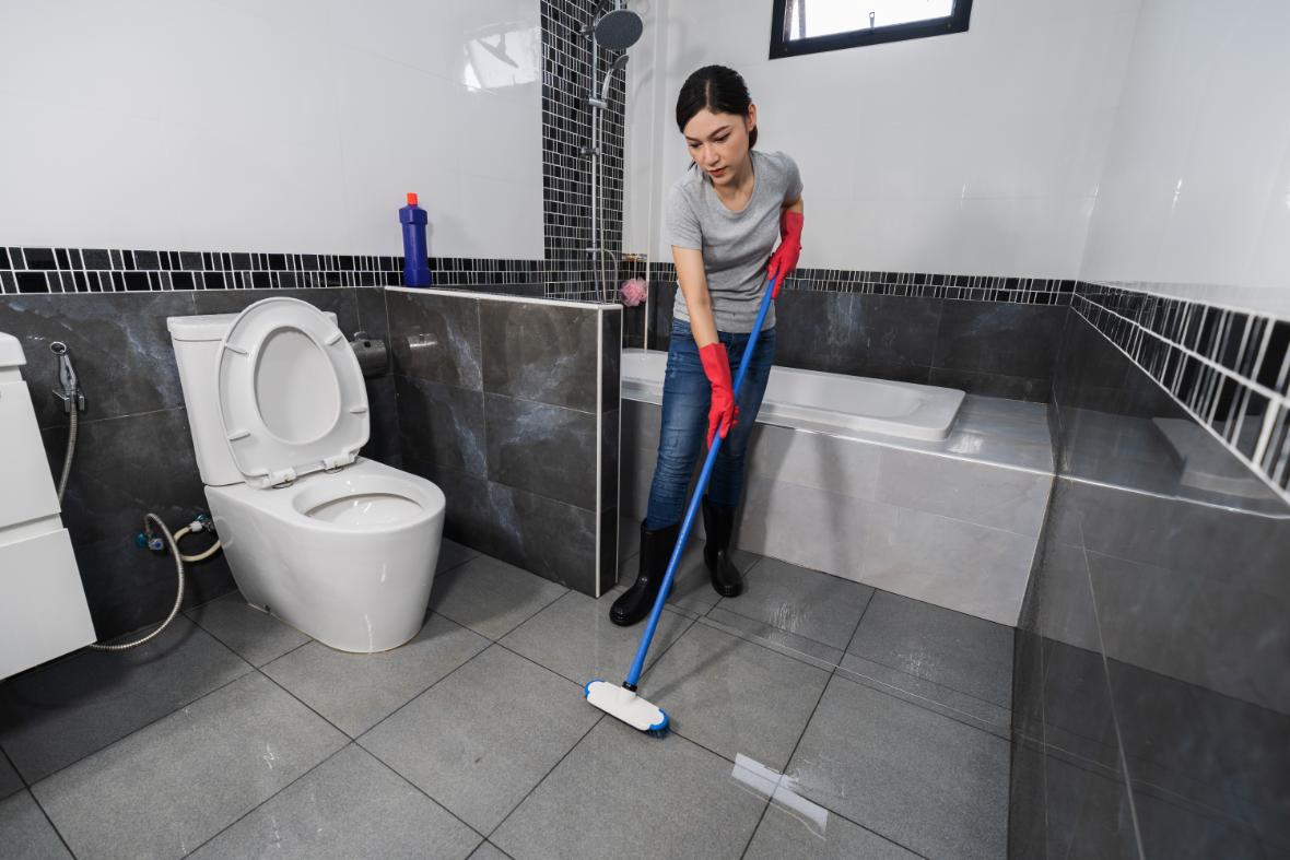 femme qui nettoie un plancher en céramique avec une serpillère dans une salle de bain
