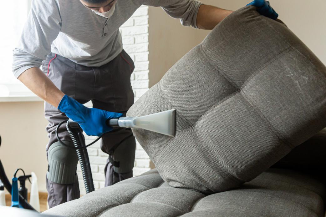 homme professionnel qui nettoie un canape rembourre avec un aspirateur. Nettoyage de meubles a domicile avec Oceanick Nettoyage au Québec