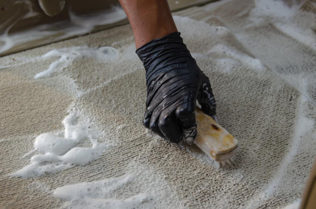 professionnel avec un gant noir qui nettoie et desinfecte un tapis avec une brosse et du produit adapte oceanick nettoyage specialiste en nettoyage a quebec
